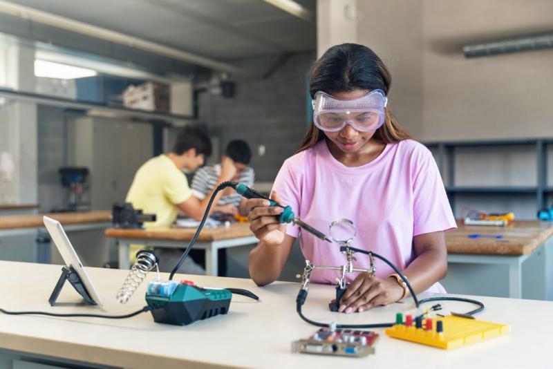 African American High School teenage Student wearing protective goggles soldering electronics circuit in a science technology workshop